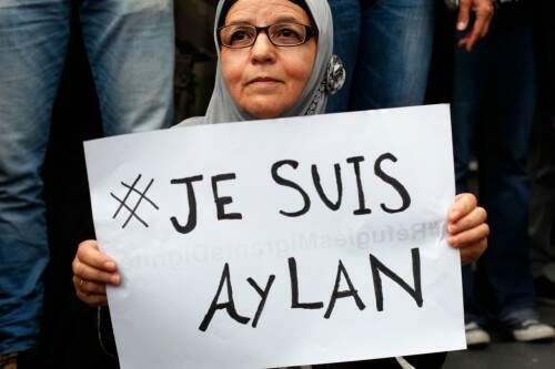 Mulher lembrou o sofrimento dos imigrantes que fogem das guerras e chegam à União Europeia com um cartaz que lembra a morte do menino Aylan Kurdi, cujo corpo foi encontrado em uma praia na Turquia. (Foto: AP)