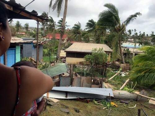 Mãe segura uma criança enquanto olha para destroços de uma casa (Foto: AFP)